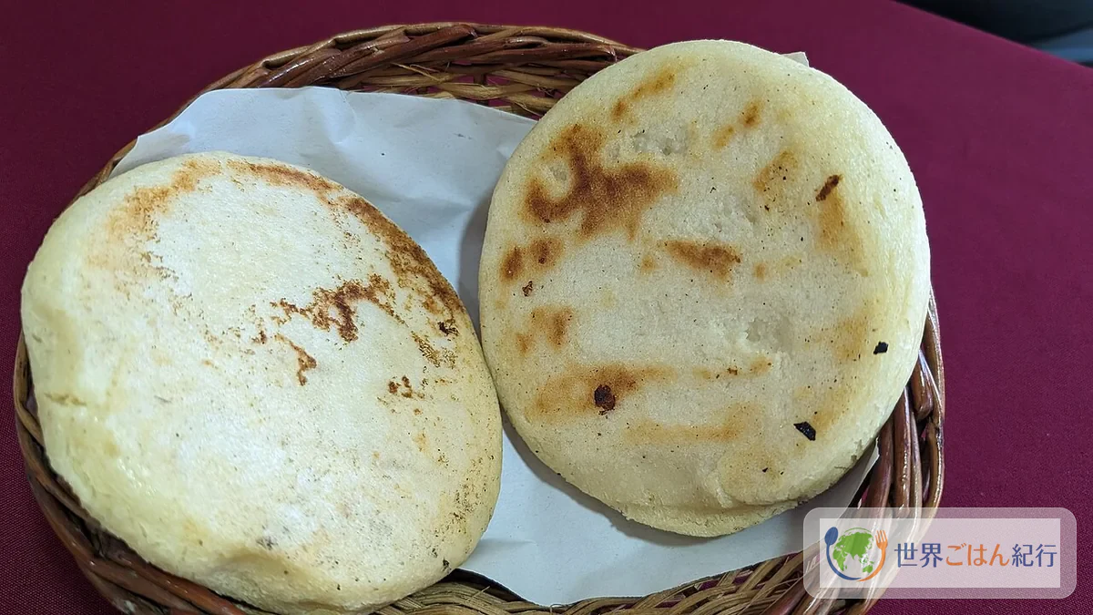 コロンビア風アレパ。白いとうもろこし生地を丸く焼き、ホガオを添えて食べる主食パン