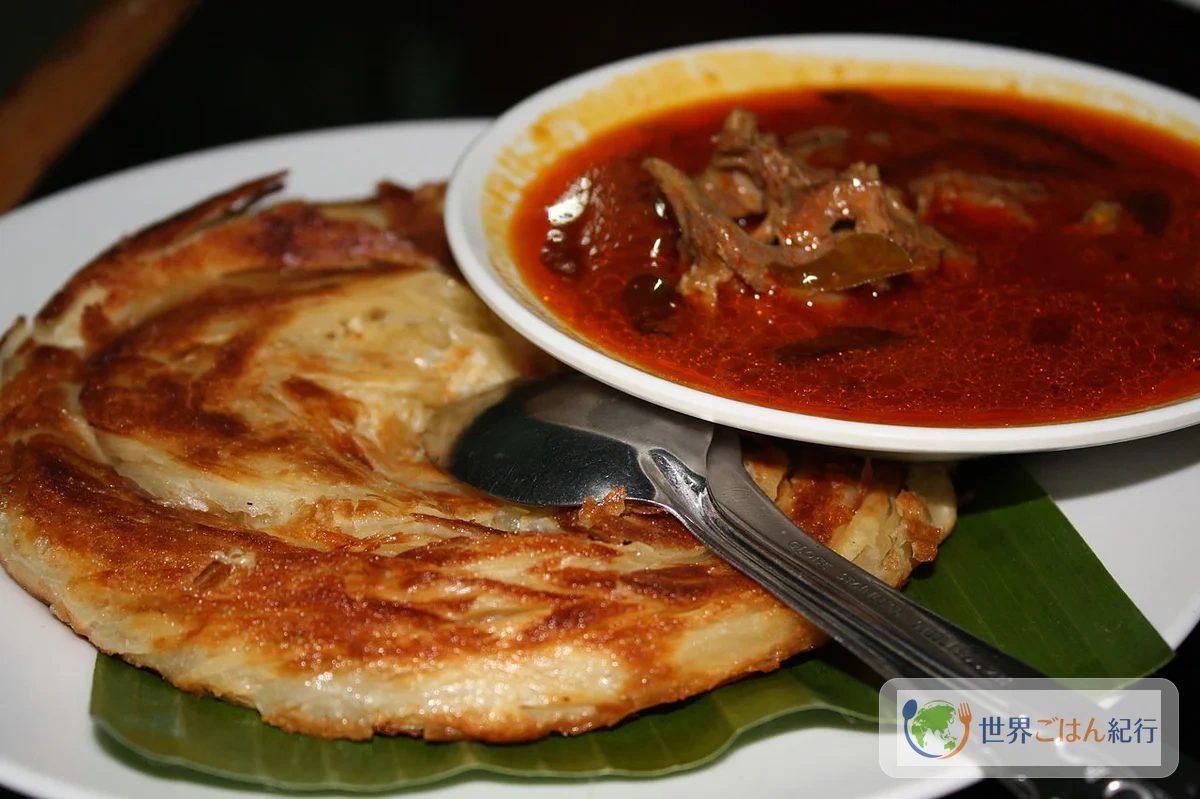 マレーシアのロティ・チャナイ。黄金色に焼き上がった層状のフラットブレッドとカレーソースが皿に盛られている