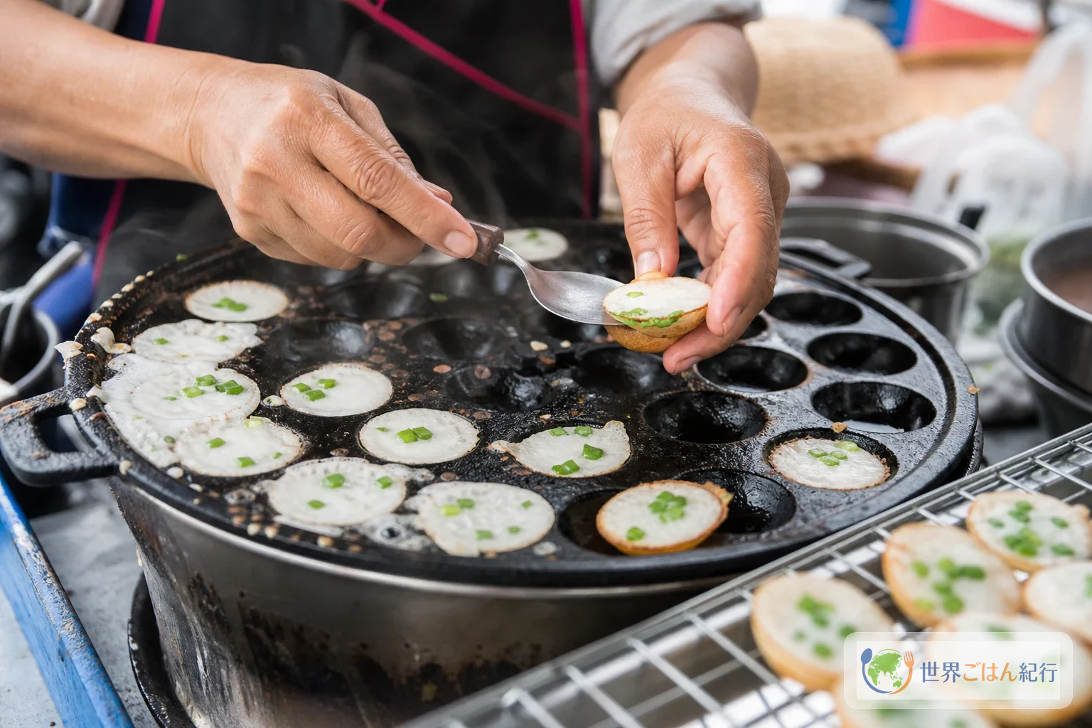 くぼみのある鉄板でカノムクロックを焼き、青ねぎをのせている場面